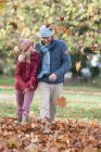 Батько і дочка обманюють в парку, прогулюючись крізь осіннє листя — стокове фото