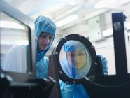 Científicas con ropa protectora revisando un filtro láser en un laboratorio - foto de stock