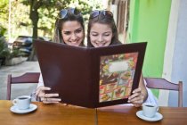 Mujeres amigas mirando el menú de la cafetería juntas - foto de stock