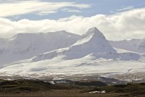 Vista panorámica de montañas cubiertas de nieve y cielo nublado, Islandia - foto de stock