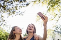 Two teenage girls in park taking smartphone selfie — Stock Photo