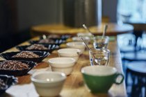 Kaffeebohnen, Schalen und Tassen auf Holztisch mit unscharfem Hintergrund — Stockfoto
