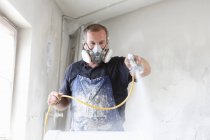 Чоловік в захисній масці розпилює фарбування деревини — стокове фото