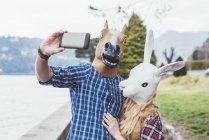 Casal usando máscaras de cavalo e coelho levando selfie smartphone, Lago de Como, Itália — Fotografia de Stock