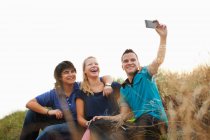 Teenagers sitting on sand dune taking self portrait photograph — Stock Photo