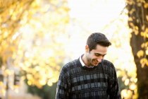 Молодий чоловік дивиться вниз в сонячному парку, посміхаючись — стокове фото