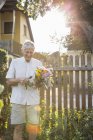 Старший чоловік в саду, тримає купу свіжих порізаних квітів — стокове фото