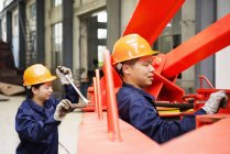 Trabajadores que utilizan equipos en instalaciones de fabricación de grúas, China - foto de stock