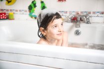 Хлопчик сидить у ванні, бульбашки на голові, посміхається — стокове фото