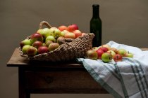 Корзина яблок и вина на столе — стоковое фото