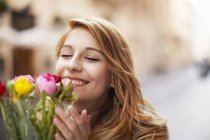 Усміхнена молода жінка пахне купою квітів — стокове фото
