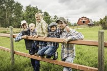 Familia multi generación de pie detrás de la cerca en la granja mirando a la cámara sonriendo - foto de stock