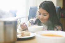 Menina comendo tigela de sopa na cozinha — Fotografia de Stock