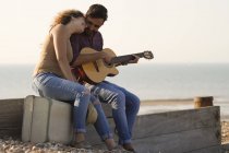 Jeune couple sur la plage, homme jouant de la guitare — Photo de stock
