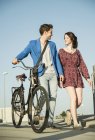 Молода пара штовхає велосипед вздовж вулиці — стокове фото