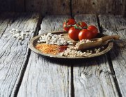Lenticchie rosse, fagioli di burro, piselli spaccati, pomodori di zafferano e vite su piatto di legno — Foto stock