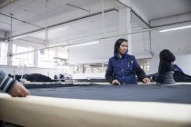 Trabajadores de fábrica desenrollando textiles en mesa de trabajo en fábrica de ropa - foto de stock