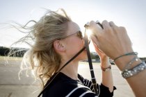 Femme adulte moyenne avec des cheveux volants prenant des photos sur appareil photo vintage — Photo de stock