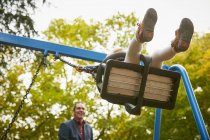 Low angle view of father pushing daughter on playground swing — Stock Photo