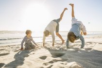 Padre e figli sulla spiaggia facendo stand — Foto stock