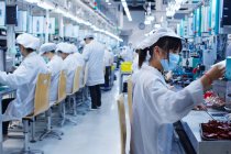 Gruppe von Arbeitern in einer Kleinteilefabrik in China, die Schutzkleidung, Hüte und Masken tragen — Stockfoto