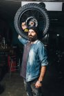 Portrait of mature man, in garage, holding motorcycle tire — Stock Photo