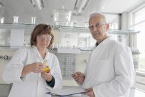 Cientistas que trabalham em laboratório, segurando líquido amarelo no frasco para injetáveis — Fotografia de Stock
