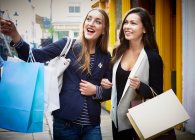 Young women arm in arm, carrying shopping bags down street — Stock Photo