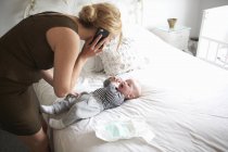 Mother talking on mobile phone and taking care of newborn baby boy, diaper changing — Stock Photo