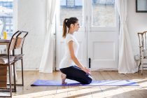 Jeune femme pratiquant le yoga position à genoux dans l'appartement — Photo de stock