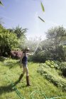Vista lateral da mulher madura no jardim esguichando água no ar com mangueira — Fotografia de Stock