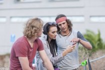 Tre giovani amici adulti che guardano smartphone sulla strada della città — Foto stock