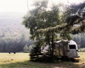 Trailer parked under tree in field — Stock Photo