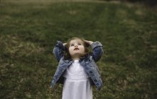 Chica joven con las manos en la cabeza mirando hacia arriba en el prado - foto de stock