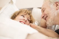Пара улыбается и смотрит друг на друга, лежа в постели — стоковое фото