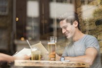 Window view of young man reading menu in restaurant — Stock Photo