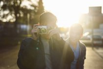 Young man taking camera photographs on sunlit street — Stock Photo
