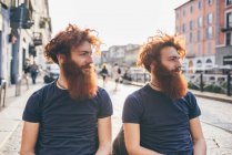 Gemelos hipster masculinos jóvenes con pelo rojo y barba en la calle de la ciudad - foto de stock