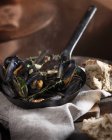 Mussels with herbs in frying pan and bread on table — Stock Photo