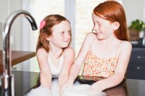 Lächelnde Mädchen spülen Geschirr im Spülbecken — Stockfoto