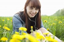 Portrait de jeune femme dans les écouteurs dans le domaine des pissenlits — Photo de stock