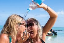 Mujer madura turista vertiendo agua sobre su amigo en la playa, Isla Reunión - foto de stock