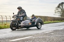 Senior man and grandson riding motorcycle and sidecar along rural road — Stock Photo