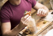 Cropped shot of young man eating burger in restaurant — Stock Photo