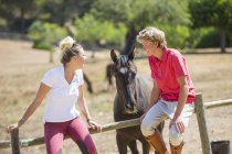 Young male and female grooms sitting on paddock fence at rural stables — Stock Photo