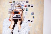 Молода жінка перед фотошпалерами фотографується на ретро камеру — стокове фото