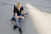Жінка скейтбордистка сидить на скейтборді — стокове фото