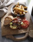Homemade bacon burger with chips on wooden board — Stock Photo