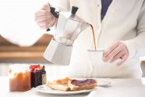Обрезанный снимок молодой женщины, наливающей кофе на завтрак — стоковое фото