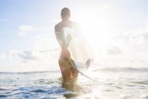 Rear view of woman carrying surfboard in sunlit sea, Nosara, Guanacaste Province, Costa Rica — Stock Photo